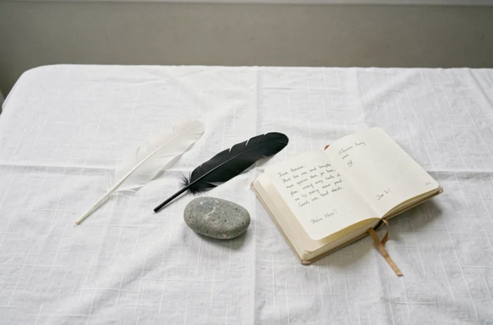 Mise en scène minimaliste avec une plume blanche, une plume noire, une pierre et un journal ouvert, évoquant la signification des contraires