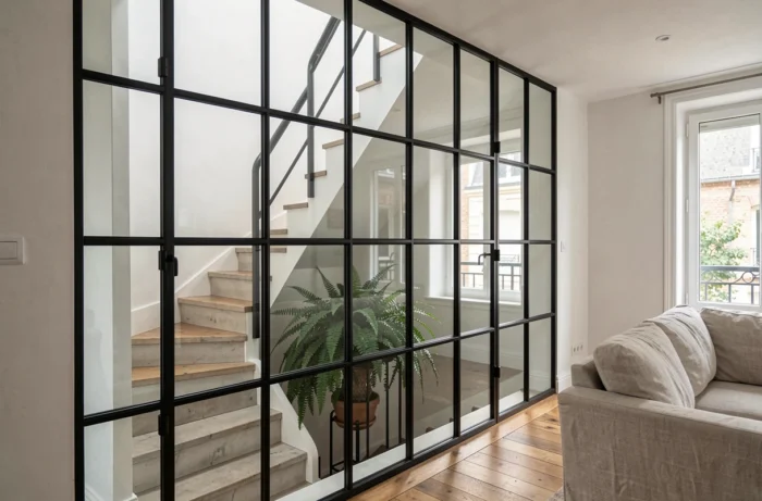 Verrière d'atelier en acier noir entre cage d'escalier et salon d'un appartement rénové